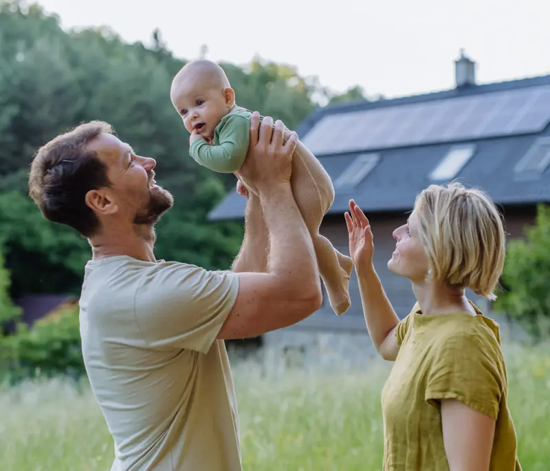 A couple lifting their baby in the garden of a home with solar panels