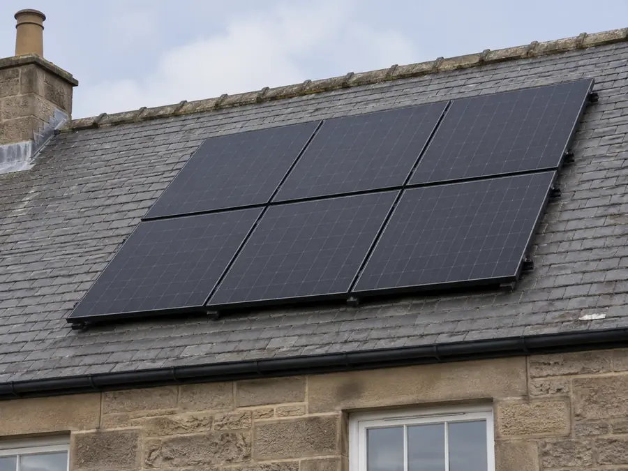Six black solar panels on the slate roof of a sandstone house